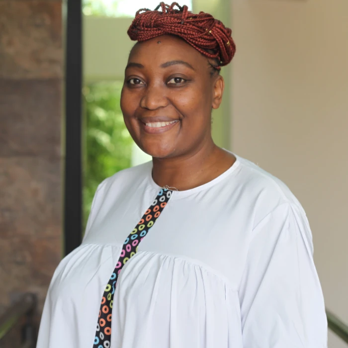Memory Kachambwa wears a white dress and has her hair in a high bun, with a gentle smile on her face.