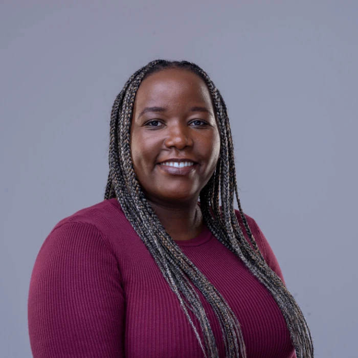 Irene Mwendwa, with lilac-grey braids is central in the image. Irene wears a burgundy longsleeve top.
